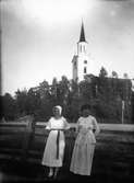 Porträtt av två flickor, Hamrånge kyrka i bakgrunden.
Originaltext: Siri och Cissi utanför Hamrånge kyrka den söndag vi åkte häst där under en Wittersjösommar.