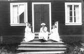 Tre kvinnor sittande på trappan till timrad byggnad.
