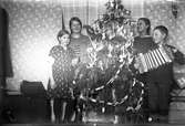 Fyra barn vid julgran, en spelar dragspel.