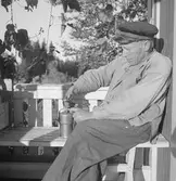 Sittande på en bänk i farstukvisten.




