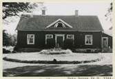 Manbyggnaden, knuttimrad, klädd med panel av stående brädor med täcklister, tak av enkupigt tegel. Rödmålad med vita dörr- och fönsterfoder samt vit taklist. Dörren ut till terrassen i vinkeln mellan själva huset och tillbygget utfört nyligen. (1944)
