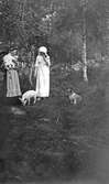 Ester Bauer och en annan kvinna står i en skogsglänta med var sin kattunge i famnen. De har också sällskap av en griskulting och en hund.