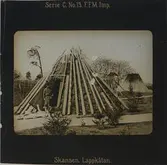 Samevistet, torvkåta. I öppningen till kåtan står en man iklädd samisk dräkt samt en hund.