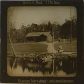 Morastugan på Skansen. I förgrunden svandammen. Personer iklädda folkdräkter samt ett par getter i miljön runt gården.