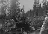 Två skogsarbetare, med skottkärra, varav den ene ligger i skottkärran.