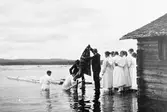 Aspiranter färdiga att en efter en mottaga dopet.
Båthuset som skymtar tillhörde Bergviksgården.