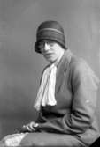 Ateljébild på en kvinna i hatt, kappa och glasögon. Enligt Walter Olsons journal är bilden beställd av Einar Andersson.