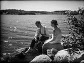Man och kvinna sittande på stenar vid vattnet , Östhammar, Uppland