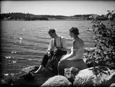 Man och kvinna sittande på stenar vid vattnet , Östhammar, Uppland