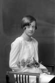 Ateljébild på en flicka med blomma och pärlhalsband. Enligt Walter Olsons journal är bilden beställd av Stina Johnsén.