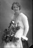 Ateljébild på en kvinna ihållandes en blombukett. Enligt Walter Olsons journal är bilden beställd av fröken K Kalmlund.