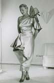 Modell i klänning av Jacques Griffe med stora garneringar vid axeln och höften.