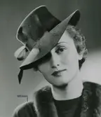 Modell i hatt med kulle och brätte. Band trätt genom kullen.