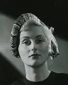 Porträtt av modell i fyrfärgad hatt med band och pärlörhängen.