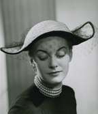 Porträtt av modell i hatt med flor och pärlhalsband, av Gilbert Orcel.