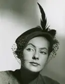 Porträtt av modell i grå velourhatt, dekorerad med flor och fjäder.