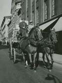 Hästdragen vagn med järnskodda hjul, sannolikt utanför Nordiska Kompaniet.  På kuskbocken två män. Text med blyerts på baksidan: 
