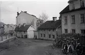Orig. text: Nygatan vid Barnhemsgatan (Nuvarande Drottninggatan).

Från vänster Systrarna Pettersons gård, Anderska gården.
Systrarna Pettersons gård: Byggnaden är flyttad till Gamla Linköping från Nygatan 58. Byggnaden är uppförd 1841. Då flyttade hemmansägaren Peter Larsson med familj in. Peters dotter Maria och senare hennes tre döttrar återvände till gården på äldre dar och den sista överlevande dottern, Sigrid, donerade byggnaden till Gamla Linköping.
Anderska gården: Byggnaden är ett lofthus med inbyggd svalgång. Det äldsta kända dokumentet rörande gården är från 1784. Gården har ägts av bl. a. fyra kakelugnsmakare och en hovrättskommissarie. 1874 flyttade Samuel Andersson in och öppnade affär i byggnaden, hans son Knut Ander (1873-1908) var en lovande konstnär. Byggnaden flyttades 1958 till Gamla Linköping.