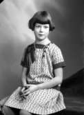 Ateljébild på en flicka i halsband och klänning. Enligt Walter Olsons journal är bilden beställd av Ingrid Karlsson.