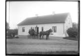 Lännäs Gästgivaregård, 1700-tals byggnad. Ett par hästar spända för droskan. En kusk och två åkande. 
Tresidig gårdsbildning.
Karl Pettersson