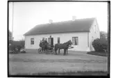 Lännäs Gästgivaregård, 1700-tals byggnad. Ett par hästar spända för droskan. En kusk och två åkande. 
Tresidig gårdsbildning.
Karl Pettersson