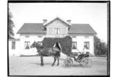 Tvåvånings bostadshus.
Häst förspänd droska med kusk.
Karl Persson