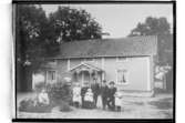 En och en halvplans bostadshus med veranda i snickarglädje. 9 personer framför huset.
Aug. Andersson
(Reproduktion 1934)