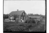 En och en halvvånings bostadshus med glasad veranda. Ekonomibyggnader. Fyra personer framför bostaden.
Josef Burén