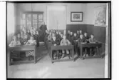 Sköllersta skola, klassrumsinteriör, 30 skolbarn sittande i skolbänkar och en lärare.
Organist A. W. Hellström