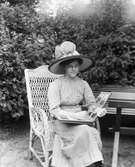 Kvinna sitter i trädgårdsstolen tittandes i ett fotoalbum






