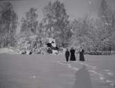 Tre personer står i snön utanför Tuna gård 1913.