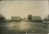 Två symmetriskt lagda byggnader vid början av gatan från landsvägen till landsvägen. Till vänster vagnbod, till höger stall.