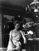 Ung kvinna i underklänning sittandes vid ett bord i en salong