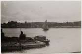 Vy över Saltsjön från Beckholmen, 1920-tal. I förgrunden del av docka på Beckholmsvarvet med förtöjd arbetsbåt, på sjön segelskuta; t v i bakgrunden Danvikshemmet och Saltsjö kvarn.
