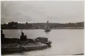 Vy över Saltsjön från Beckholmen, 1920-tal. I förgrunden del av docka på Beckholmsvarvet med förtöjd arbetsbåt, på sjön segelskuta; t v i bakgrunden Danvikshemmet och Saltsjö kvarn.
