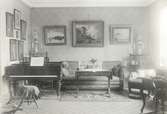 En salong med bland annat tavlor, piano och soffa.