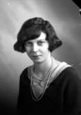 Ateljébild på en kvinna i pärlhalsband och klänning. Enligt Walter Olsons journal är bilden beställd av fröken Gunhild Pettersson.