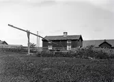 Mangårdsbyggnad med brunnsvipp. Huset är en tvåvånings enkelstuga, troligen påbyggd eftersom övervåningens fönster sitter just under takfallet.