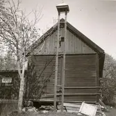 En ekonomibyggnad med timmervägg och vällingklocka.