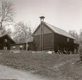 En ekonomibyggnad med timmervägg och vällingklocka.
