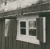 Detaljfoto av en stuga med torvtak och fönsterluckor i hembygdsarken Ekbacken.