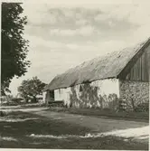 Ekonomibyggnad med stråtak uppförd i sten.