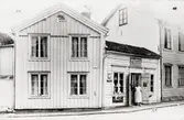 Affärexteriör. Alma Johanssons matvaru- och diversehandel i hörnet Molinsgatan-Västerlånggatan.
I dörren står fröken Alma Johansson som köpte affären 1917 och hade den fram till i början av 1960-talet.