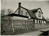 Ett bostadshus med mansardtak år 1908. Runt byggnaden finns ett staket.