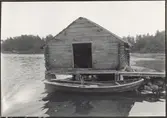 Fiskebod med brygga och båt. Sedd från väster.