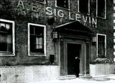 Entrén till AB Sig. Levin.
Grundad 1863 av Simon Levin. Firman bedrevs då som handelsrörelse. År 1938 ombildades firman till AB med Sig. Fürstenberg som direktör. Fabriksmässig konfektion började 1927 och flyttades till Smedjegatan 1949, där en modern syfabrik uppfördes. ( Se Minnesskrift - Stadsfullmäktige i Kalmar 1863-1962)
