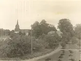 Parti från trädgården vid Tuna gård med kyrkan och en av flyglarna i lunden.
