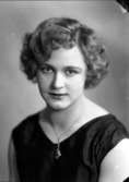 Ateljébild på en kvinna i klänning och halsband. Enligt Walter Olsons journal är bilden beställd av Margit Magnusson.