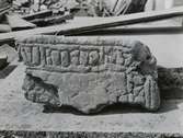 Böda kyrka. Fragment av gravflisa med majuskler, funnen vid gravar, under sakristians mur, utanför östväggen, när man grävde för värmekammare 1931.