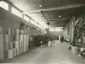 Kalmar Nya Tapetfabrik. Pårullning i en fabrikshall. Tapetrullar till vänster.